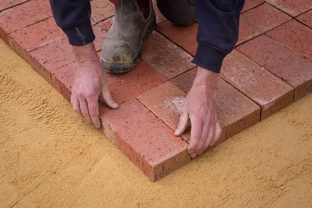 Worker laying brick pavers on a sand base